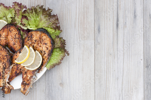 Fried salmon on a white plate decorated with lemon and salad