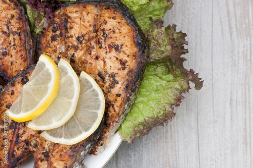 Fried salmon on a white plate decorated with lemon and salad