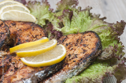 Fried salmon on a white plate decorated with lemon and salad