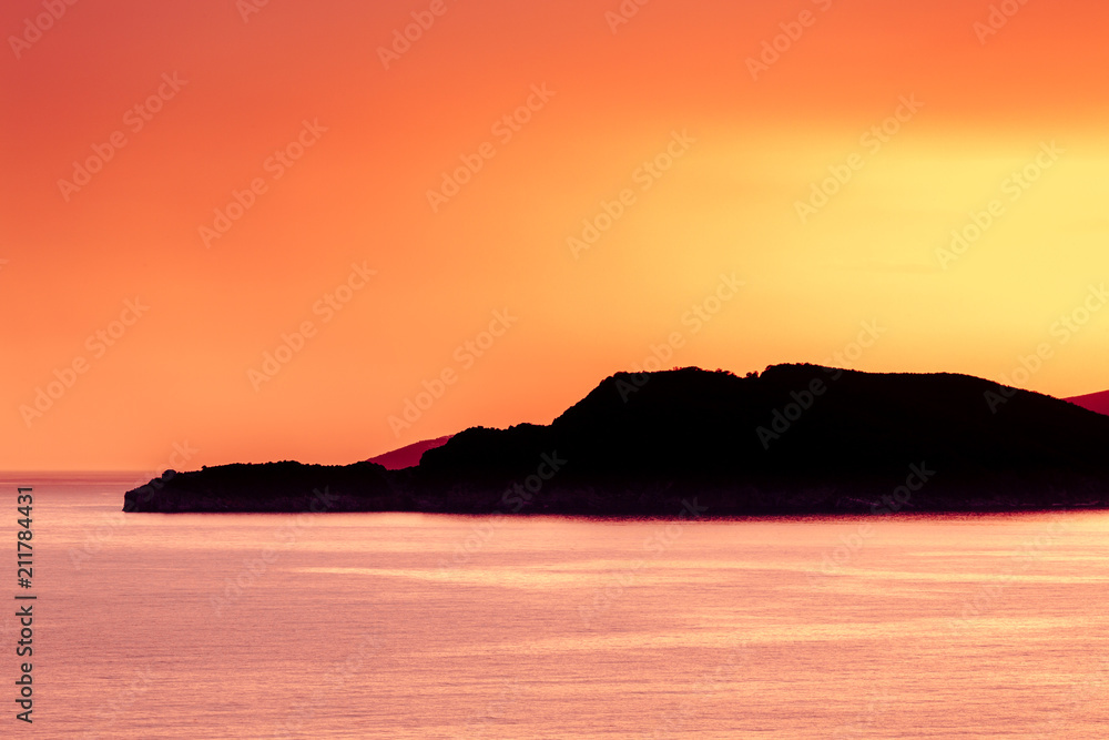 Warm summer sunset over the sea with clear sky in Montenegro with an island silhouette