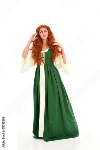 full length portrait of red haired girl wearing long green medieval gown. standing pose  isolated on white studio background.