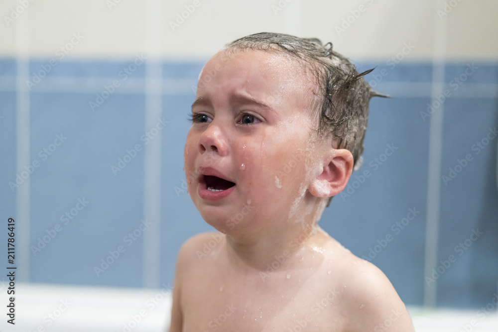 Crying baby by in a bathtub. Infant kid sreaming while taking a bath. baby cries in the bathroom Crying baby by in a bathtub. Infant kid sreaming while taking a bath. baby cries in the bathroom