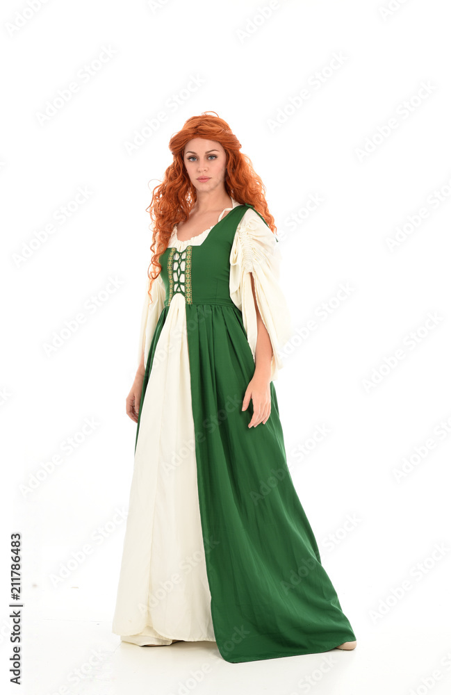 full length portrait of red haired girl wearing long green medieval gown. standing pose, isolated on white studio background. full length portrait of red haired girl wearing long green medieval gown. standing pose, isolated on white studio background.