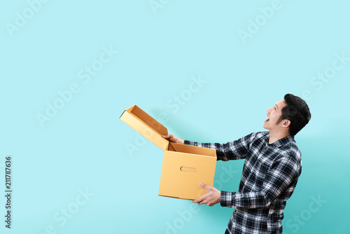 Side view of happy customer asian man smiling opening and holding box looking up to copy space above with isolated blue background feeling excited and satisfaction. Ordering or buying concept design. photo