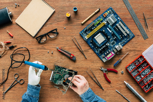 cropped image of man with prosthetic arm repairing hard drive by soldering iron