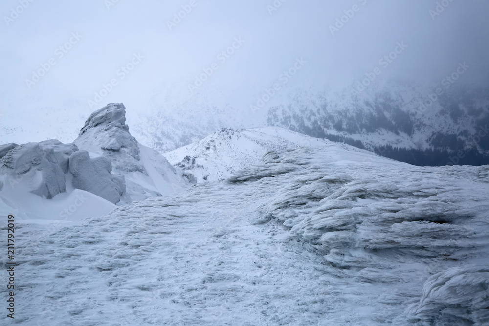 At the high mountains there are fantastic, interesting, frozen structured rocks looking like mystical fairytale figures. The panoramic view with the fog, high peaks in snow.