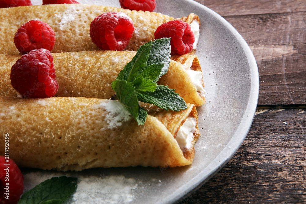 Homemade crepes served with fresh raspberrries and powdered sugar on rustic wooden table Homemade crepes served with fresh raspberrries and powdered sugar on rustic wooden table