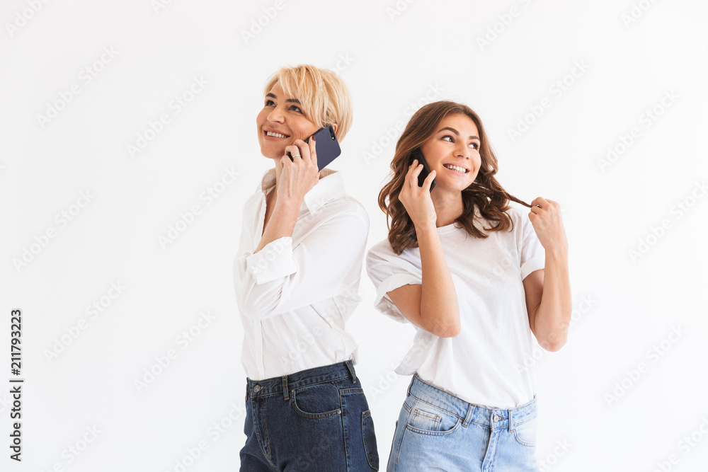 Young lady standing with her mother talking by mobile phones Young lady standing with her mother talking by mobile phones