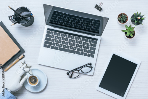 cropped image of businessman with prosthetic arm resting and drinking coffee at table with laptop in office