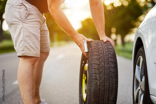 The man changes the tire to a broken car on the road