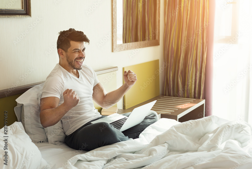 Young man using laptop while sitting on a bed Young man using laptop while sitting on a bed