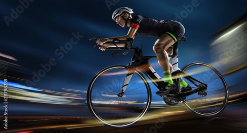 Sport background. Athletic woman cycling road bike in the evening. Dramatic view of the night city.