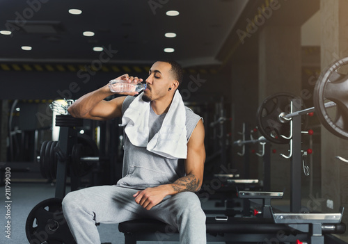 Black bodybuilder drinking water at gym photo