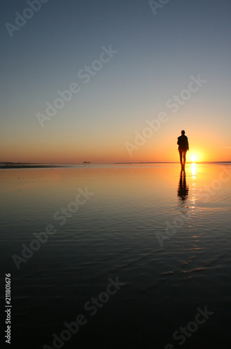 Silhouette of a woman walking on a beach with her reflection in the water