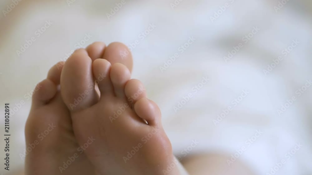 Delicate female feet moving toes playfully on white bedding Delicate female feet moving toes playfully on white bedding