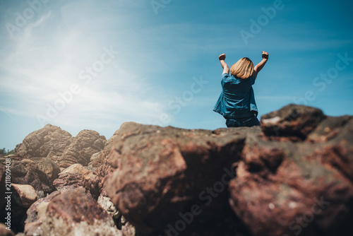 Women sitting on the rock.Strong girl confidence open arms under the beautiful sky at the seaside.