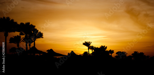 summer sunset in clouds. Golden sunset evening in mountain and sea beach. Orange sunset on mountain pick and palms on seashore with umbrellas. Hot egyptian evening and sunset.