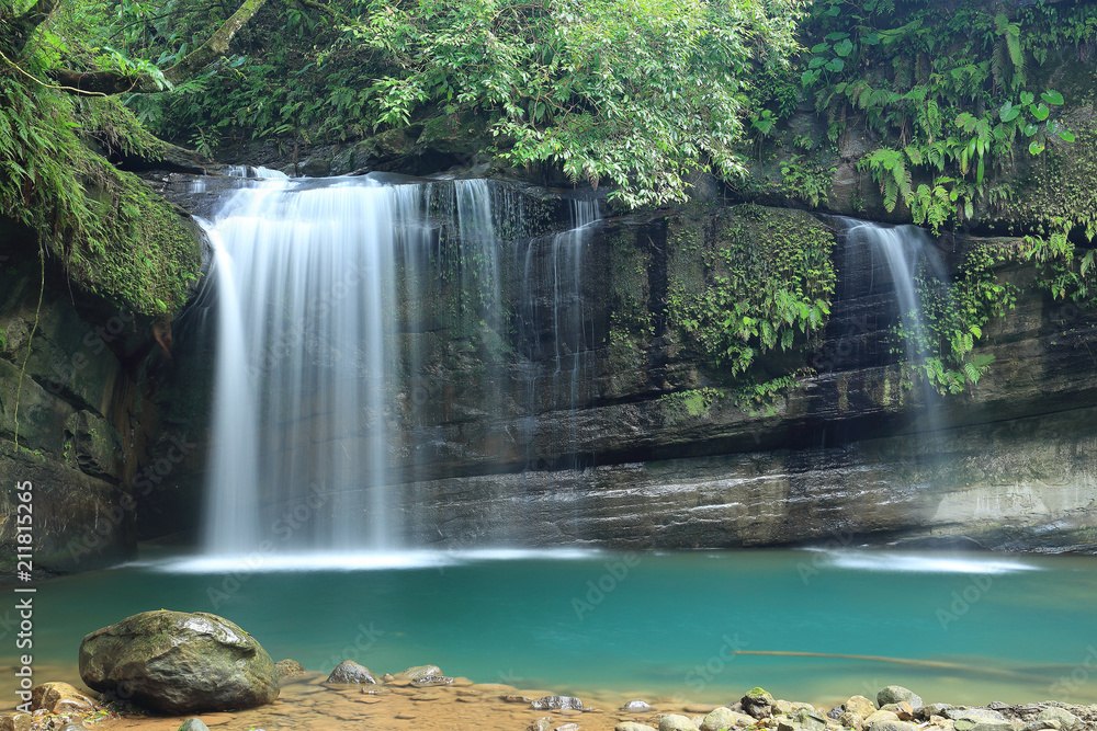 Fototapeta premium A cool refreshing waterfall tumbling down the cliff into an emerald pond hidden in a mysterious forest of lush greenery ~ Scenic view of a beautiful waterfall and intriguing river potholes in Taiwan