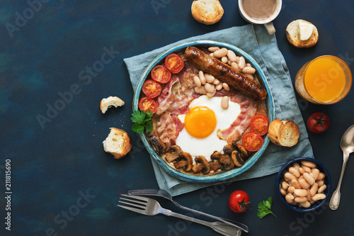 Traditional English breakfast on a blue background. Fried egg with sausage, mushrooms, beans, tomatoes and bacon. Top view, copy space.