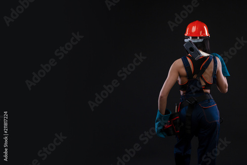 Back view of a female worker holding a hammer and helmet on black background