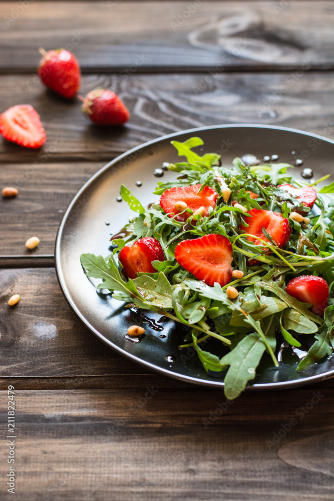 Fresh salad with arugula and strawbery with balsamic sauce and pine nuts. Vegetarian food. Salad with berries. Vitamin food, diet salad on wooden background in black plate. Fresh salad with arugula and strawbery with balsamic sauce and pine nuts. Vegetarian food. Salad with berries. Vitamin food, diet salad on wooden background in black plate.