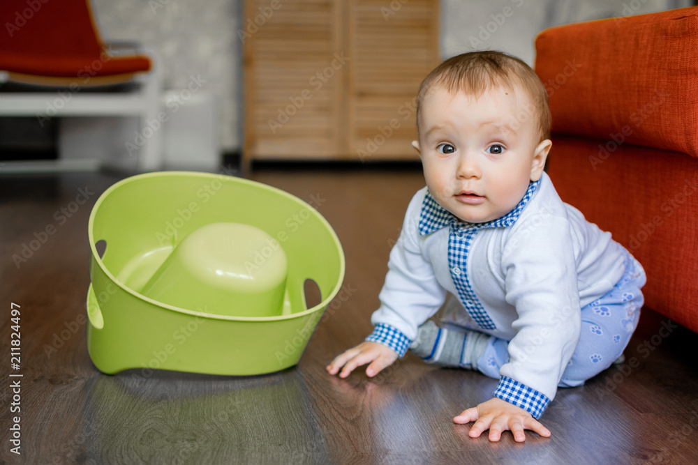 Portrait of an innocent baby boy sitting on floor in room near flipped over potty. Portrait of an innocent baby boy sitting on floor in room near flipped over potty.
