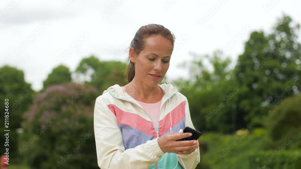fitness, sport and healthy lifestyle concept - smiling woman listening to music on smartphone at park fitness, sport and healthy lifestyle concept - smiling woman listening to music on smartphone at park
