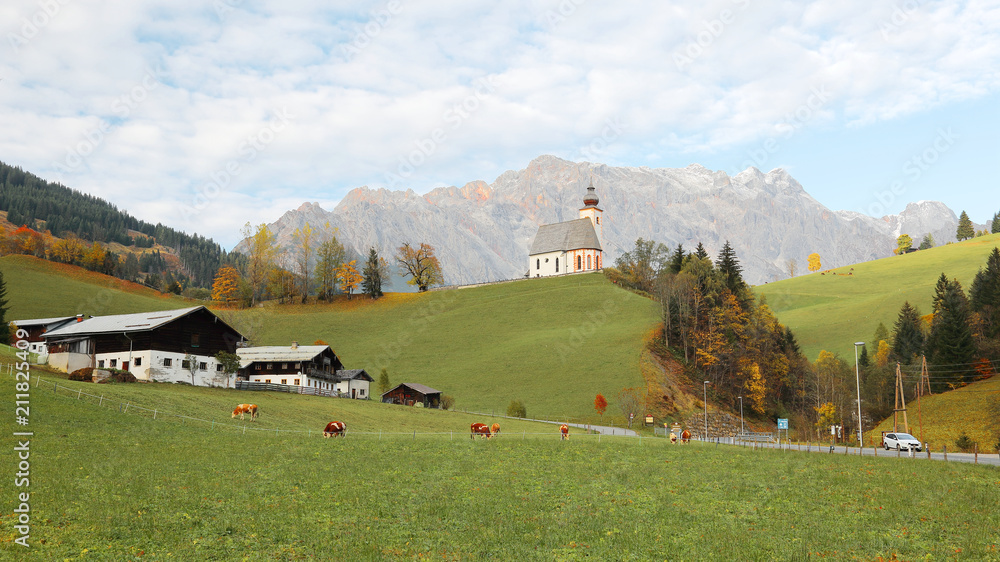A church high on hilltop with a mountain range in the background and a grassy ranch in the foreground ~ Beautiful scenery of St. Nikolaus Church of Dienten Village and Hochkoenig Mountains in Austria