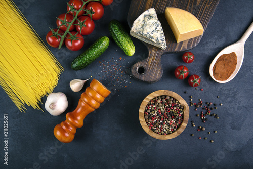 Blue cheese on wooden cutting near the peppermint,vegetables, spices and noodles on concrete background