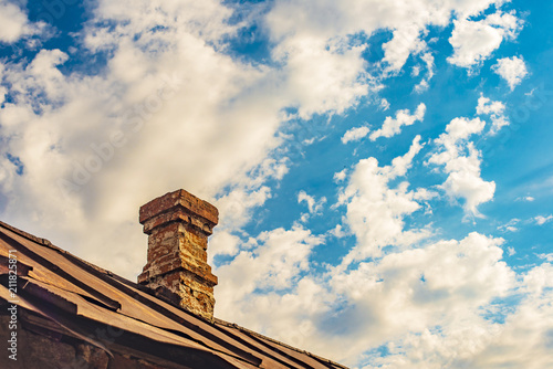 An old brick pipe on the roof of a residential building with an iron roof against a background of clouds, HDR photo