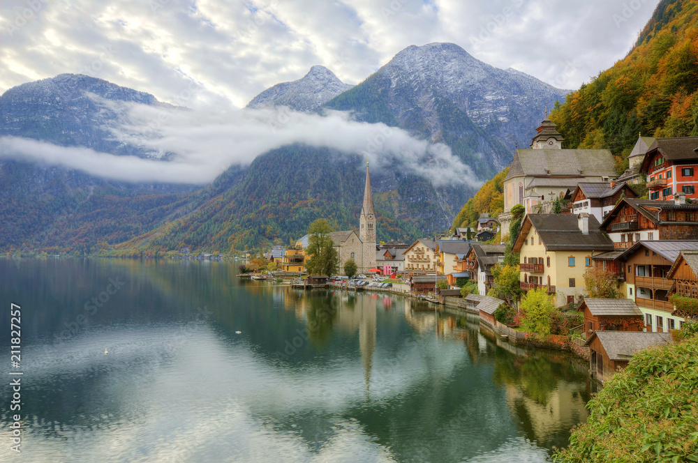 Morning view of Hallstatt, a peaceful lakeside village in Salzkammergut region of Austria, with majestic mountains reflected on lake water in colorful autumn season ~ A beautiful UNESCO heritage site