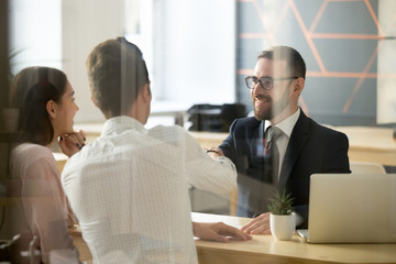 Smiling male realtor or broker shaking hand of excited buyers couple, negotiating about first house purchase or taking loan, insurance agent welcoming clients with handshake at consultation meeting