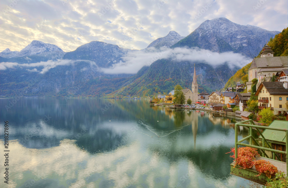 Morning view of Hallstatt, a peaceful lakeside village in Salzkammergut region of Austria, with majestic mountains reflected on lake water in colorful autumn season ~ A beautiful UNESCO heritage site