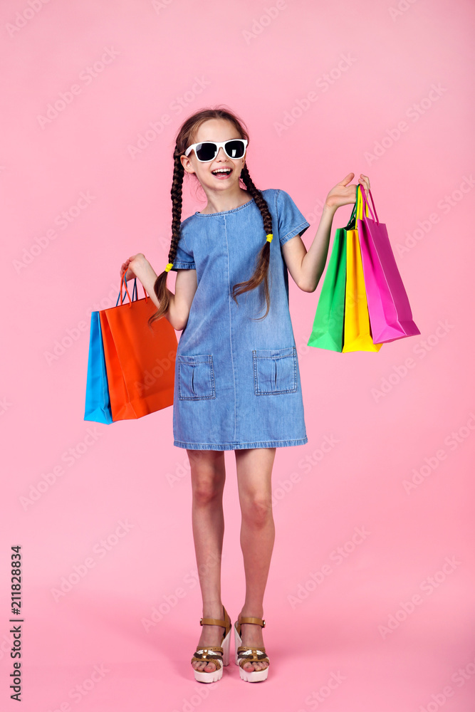 Young girl in denim dress with shopping bags on pink background