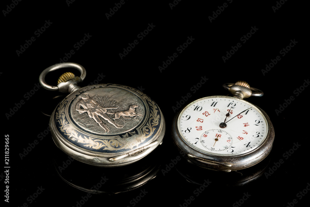 Two old pocket watches on a black reflective surface