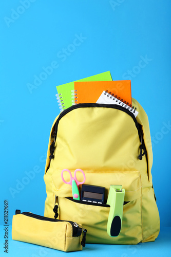 Yellow backpack with school supplies on blue background