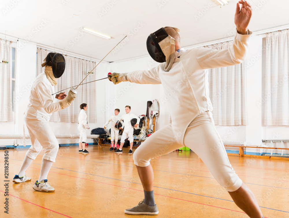 Adults and teens wearing fencing uniform practicing with foil