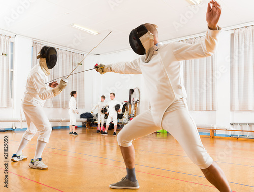 Adults and teens wearing fencing uniform practicing with foil © JackF