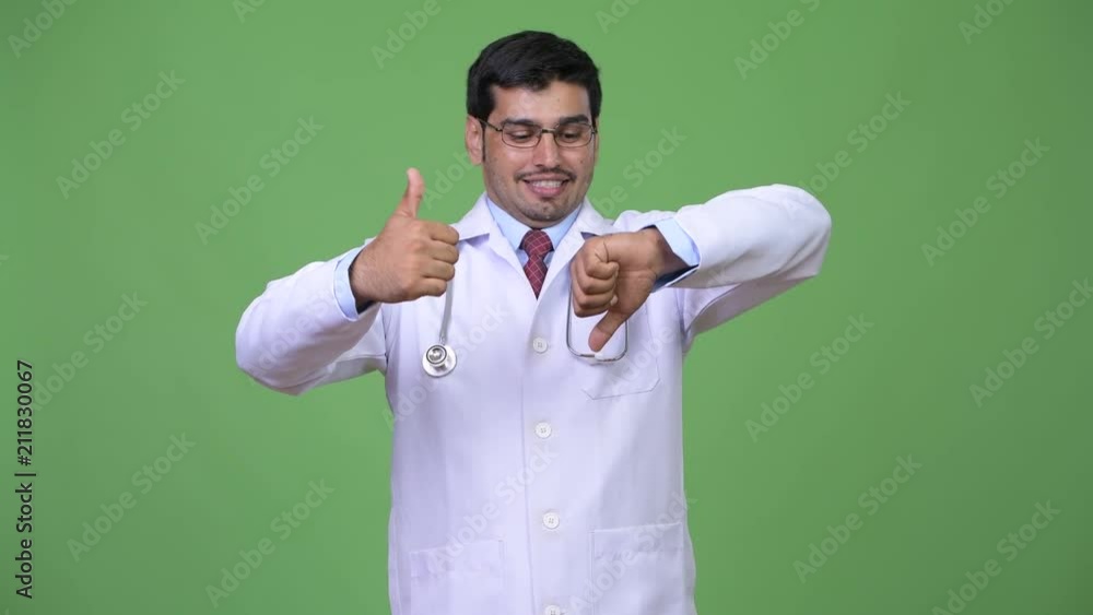 Young handsome Persian man doctor choosing between thumbs up and thumbs down Young handsome Persian man doctor choosing between thumbs up and thumbs down