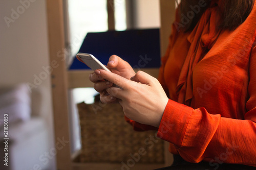 Lady using her smartphone for texting. Cropped picture of woman wearing ginger blouse holding phone in her hands typing text message.