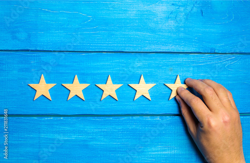 Canvas Print A hand puts the fifth wooden star on a blue background
