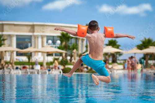 Caucasian boy having fun making fantastic jump into swimming pool at resort. Back view.