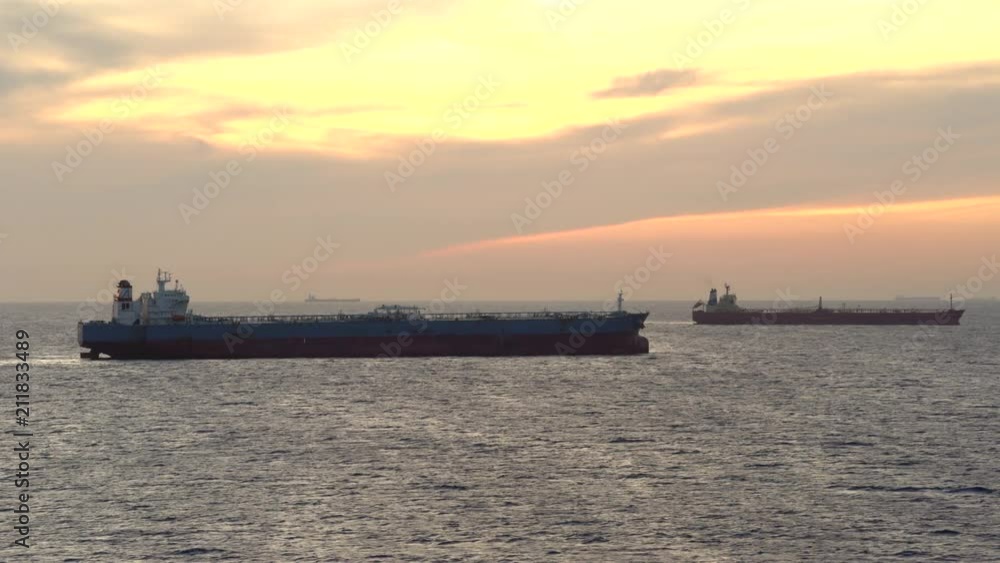 Anchored tanker, cargo ships silhouette at sunset