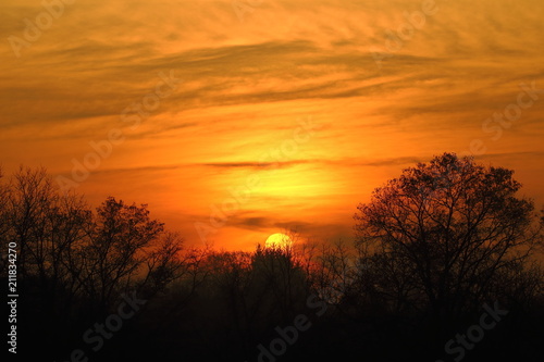 A flaming winter sunrise fills the sky with color. A light covering of clouds allows the entire disc of the sun to be visible to the naked eye creating an inspiring spectacle.