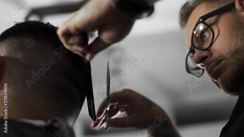 Tattoed barber makes haircut for customer at the barber shop by using scissors and comb , man's haircut and shaving at the hairdresser, barber shop photo