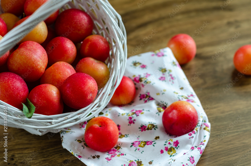 Red plum in a wicker basket on the wooden table