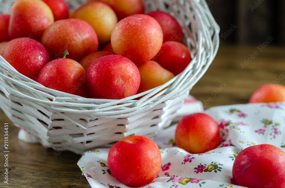 Red plum in a wicker basket on the wooden table Red plum in a wicker basket on the wooden table