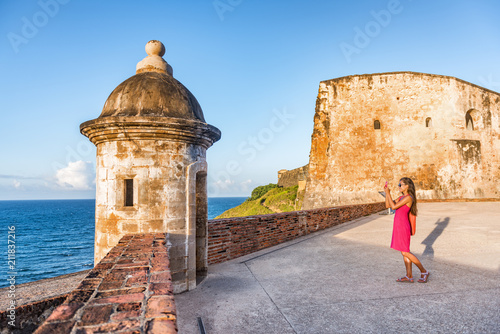 Old San Juan city tourist taking photo in Puerto Rico. Woman using phone taking pictures of ruins of watch tower of San Cristobal Castillo Fort, with ocean background. photo