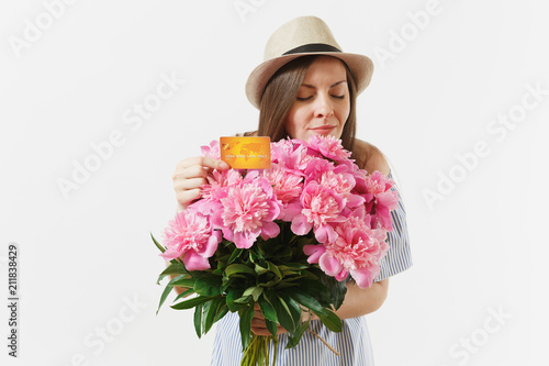 Young happy woman in blue dress, hat holding credit bank card, money, bouquet of beautiful pink peonies flowers isolated on white background. Business, delivery, online shopping concept. Copy space.