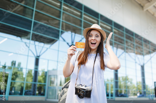 Young shocked traveler tourist woman with retro vintage photo camera, spreading hands, holding credit card at international airport. Passenger traveling abroad on weekends getaway. Air flight concept.
